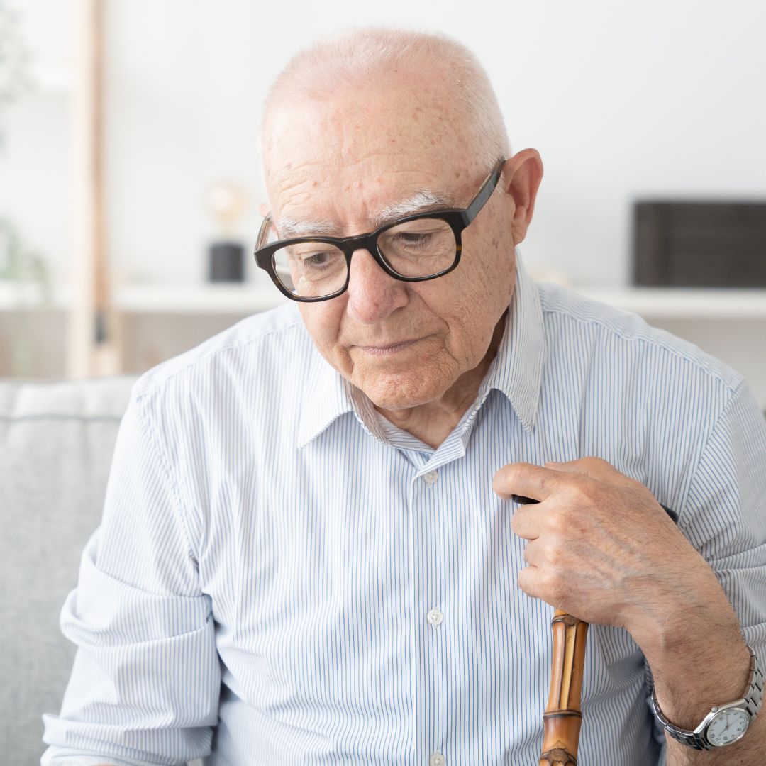 sad-looking senior holding cane on couch