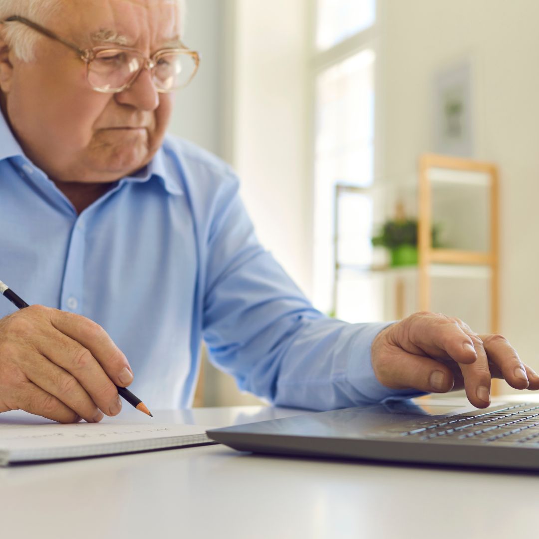 senior writing on paper and using laptop